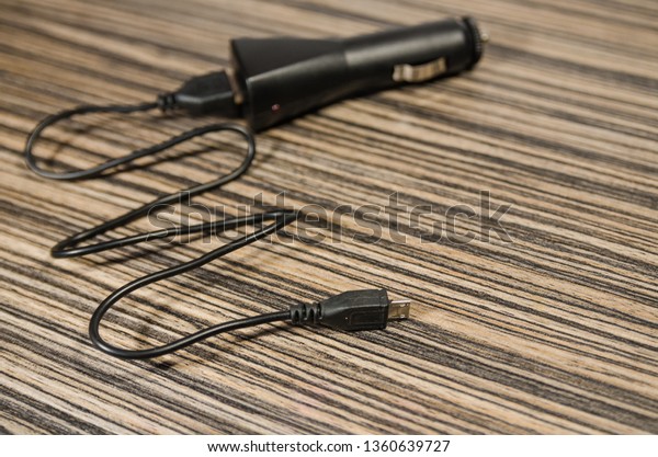 Black phone adapter for a car with a cable on\
the wooden table background. Charge your device on the way in the\
automobile.