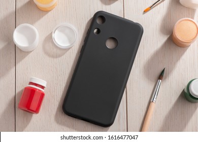 Black Phone Case, Jars Of Various Color Paint And Brushes On Wooden Table, Top View. Mockup For Your Design.