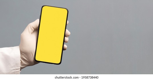 Black Phone In Doctor Hand With Yellow Screen For Mockup, Gray Background