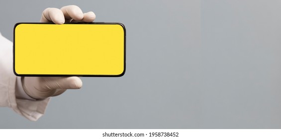 Black Phone In Doctor Hand With Yellow Screen For Mockup, Gray Background