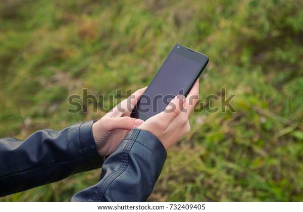 black phone in the hands of a teenager background\
of green grass