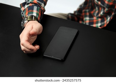 Black phone and male hand on the black table. Business concept. Top view. Close up.