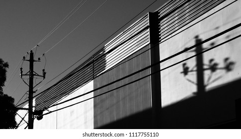 Black And Photo Of A Telephone Pole Casting A Shadow On An Industrial Building.