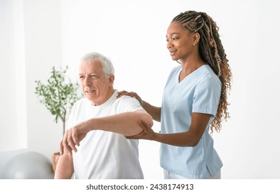 A black Physiotherapist helping senior man with in clinic. Elderly man undergoing physiotherapy treatment for injury - Powered by Shutterstock