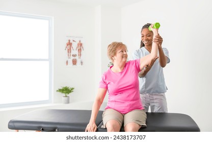 A Black physiotherapist helping senior woman in clinic. Elderly woman undergoing physiotherapy treatment for injury - Powered by Shutterstock