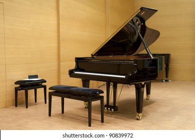 a black piano ready for playing with stool in front on a wooden stage