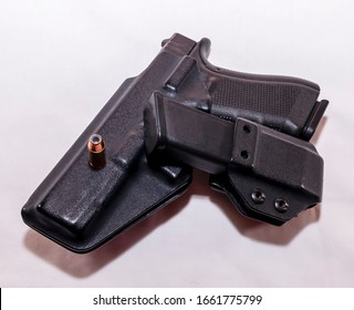 A Black Pistol In A Plastic Holster With A Loaded Magazine Holster And A Hollow Point Bullet On A White Background