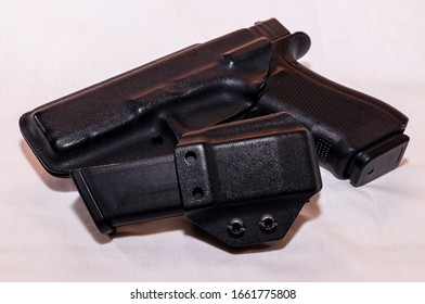 A Black Pistol In A Plastic Holster With A Loaded Magazine Holster On A White Background