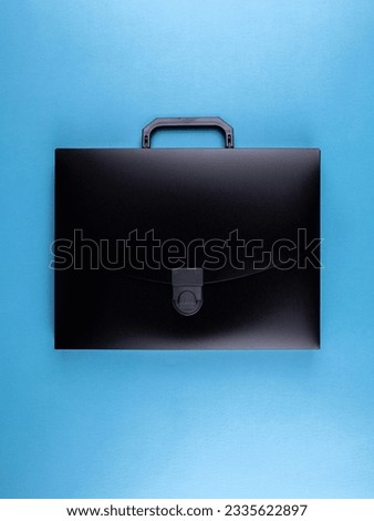 Black plastic  briefcase folder for documents and school items on a bright blue table