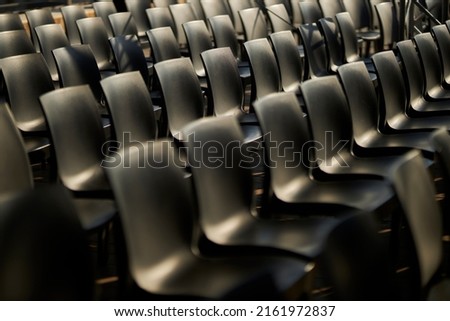 Black plastic chairs stand in rows. Black chairs with backs