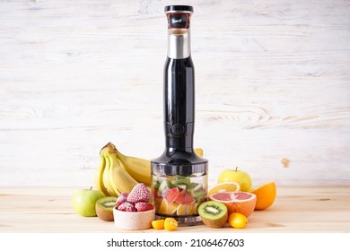 Black plastic electrical hand blender and accessories with sliced fruit on wooden background.