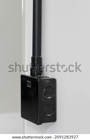The black plastic electrical junction box on white concrete wall.