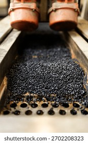 Black plastic pellets moving through a machine for industrial recycling and manufacturing