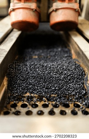 Black plastic pellets moving through a machine for industrial recycling and manufacturing