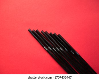Black plastic single use straws isolated on red background. Top view.