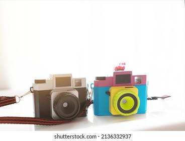 black plastic toy camera and blurred mix color cameraon shelf near window with sun light on background - Powered by Shutterstock