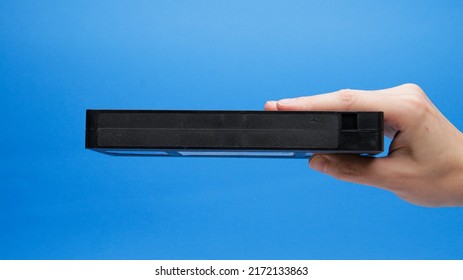 Black Plastic VHS Tape Side View In Hand On A Blue Background