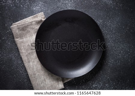 Black plate, cutlery and napkin on stone table top view. Table setting.