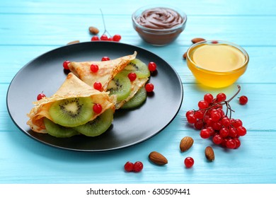 Black plate with delicious pancakes and kiwi on blue wooden table