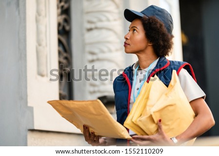 Black postwoman delivering mail in residential district. 