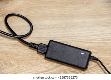 A black power adapter on a wooden surface, providing an aesthetic appeal and emphasizing modern technology. Perfect for articles about electronics and workspace setup.