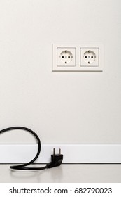 Black Power Cord Cable Unplugged With European Wall Outlet On White Plaster Wall  With Copy Space