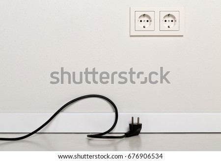 Black power cord cable unplugged with european wall outlet on white plaster wall  with copy space