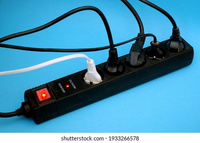 Black Power Surge Protector With Cables And Light On Blue Background. Electrical Power Strip Extension Socket, Power Extender, Surge Protector Isolated On Blue Background.