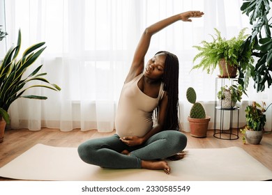 Black pregnant woman doing exercise during yoga practice at home - Powered by Shutterstock