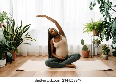 Black pregnant woman doing exercise during yoga practice at home - Powered by Shutterstock