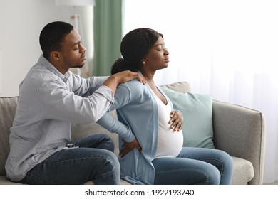 Black pregnant woman suffering from back pain at home, attentive spouse comforting her. African expecting lady having childbirth labor while sitting with husband on sofa at home, copy space - Powered by Shutterstock