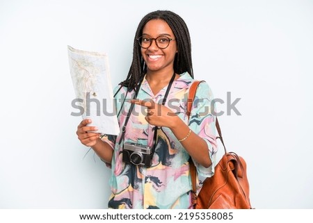 black pretty woman smiling cheerfully, feeling happy and pointing to the side. backpacker tourist with a map