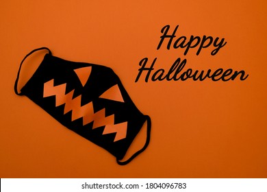 Black protective mask with orange eyes and mouth on an orange background.Happy Halloween lettering on an orange background.Halloween and covid-19 concept.Copy space for text, top view - Powered by Shutterstock