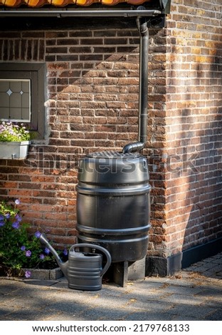 Black rain barrel with watering can to collect rainwater, water conservation concept