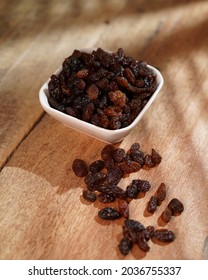 Black Raisins In White Bowl On Wooden Table. Raisin Black Is A Color That Is A Representation Of The Color Of Black Raisins.