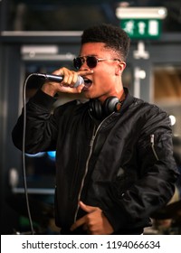 Black Rapper Performing With Microphone, Headphones Around Neck.