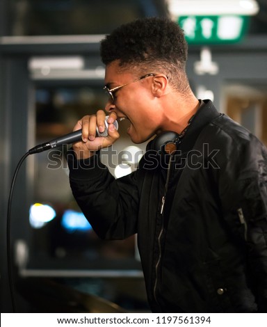 Black rapper performing with microphone. Side profile. Headphones around neck.