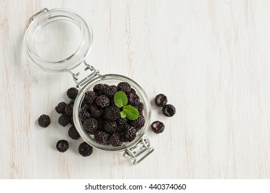 Black raspberries in a glass jar on a white wooden background