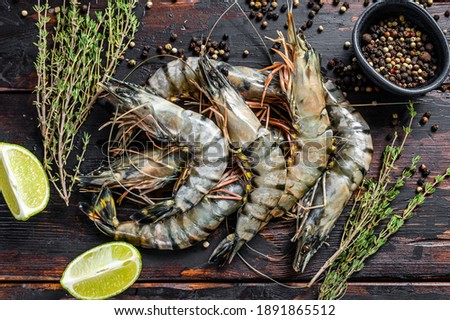 Black raw tiger prawns, shrimps with thyme and pepper. Black wooden background. Top view.