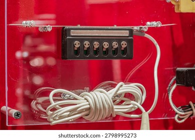 Black rectangular electrical panel featuring circular metal terminals, neatly bundled white cables secured by a metal clip, clean maintenance state, vibrant red glossy background highlighting indust.
