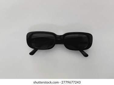 Black rectangular retro-style sunglasses with dark tinted lenses placed flat on a white surface, minimalist fashion accessory concept with soft natural lighting and subtle shadow.