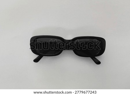 Black rectangular retro-style sunglasses with dark tinted lenses placed flat on a white surface, minimalist fashion accessory concept with soft natural lighting and subtle shadow.