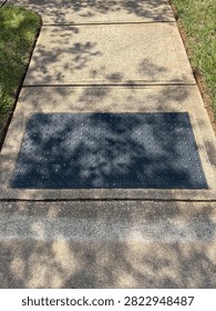 Black rectangular truncated dome panel detectable warning surface on sidewalk by the street for safety, on a sunny day with shadows 