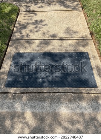 Black rectangular truncated dome panel detectable warning surface on sidewalk by the street for safety, on a sunny day with shadows 