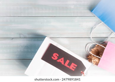 Black and red sale tag. White, blue, and pink shopping bags on a light blue-green plank background. - Powered by Shutterstock