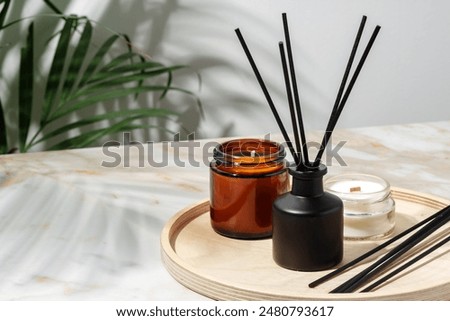 Black Reed Diffuser, Amber Candle, and Wooden Tray on White Surface