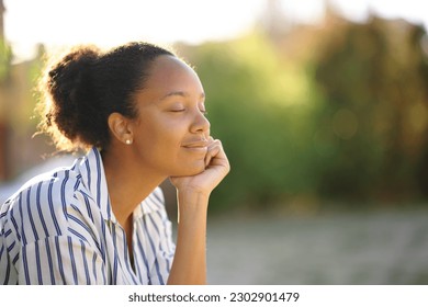 Black relaxed woman resting alone in a park at sunset