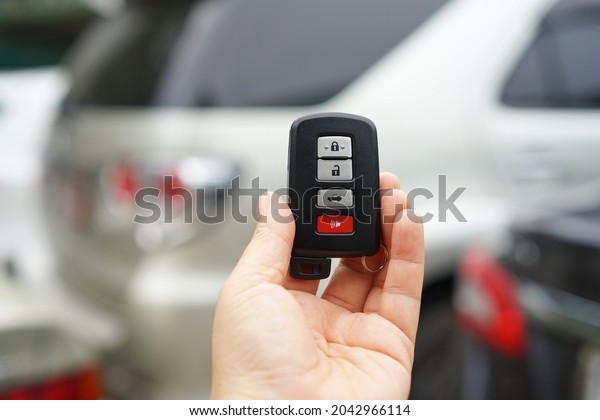 A black remote car key in the driver\'s hand with\
a small ring hanging. The remote has three gray four buttons for\
locking and unlocking the car. The red button is for the emergency\
safety system.