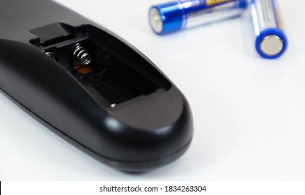 Black remote control with blue AAA batteries on a white background. Battery replacement, spare parts. Battery empty compartment of the remote control close-up.