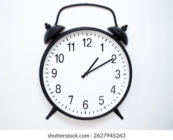 Black Retro Alarm Clock Showing 01:10 or 13:10. Classic Bell Style on White Wood Background.